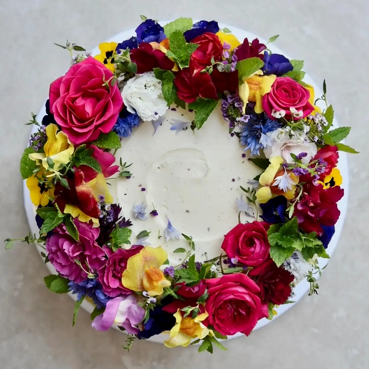 A cake decorated with multi coloured edible flowers is pictured from above