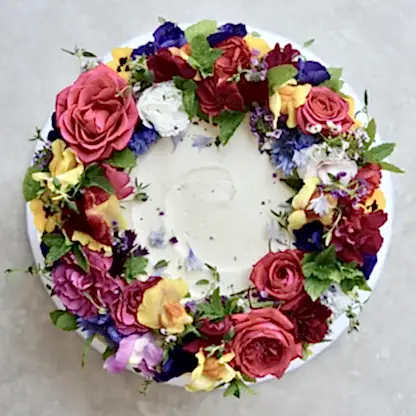 A cake decorated with multi coloured edible flowers is pictured from above 