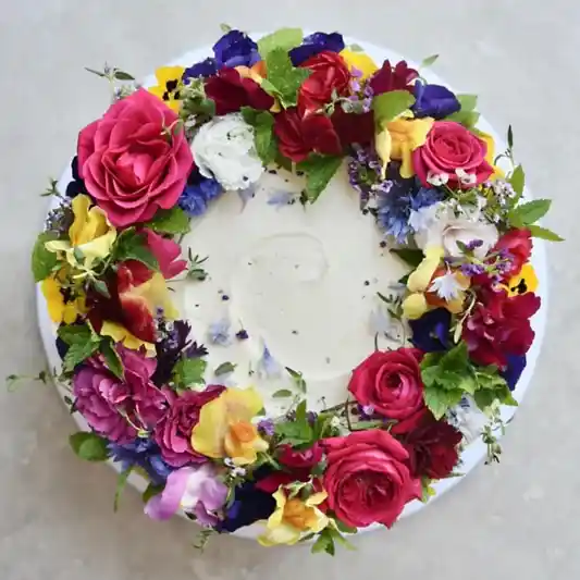 A cake decorated with multi coloured edible flowers is pictured from above 