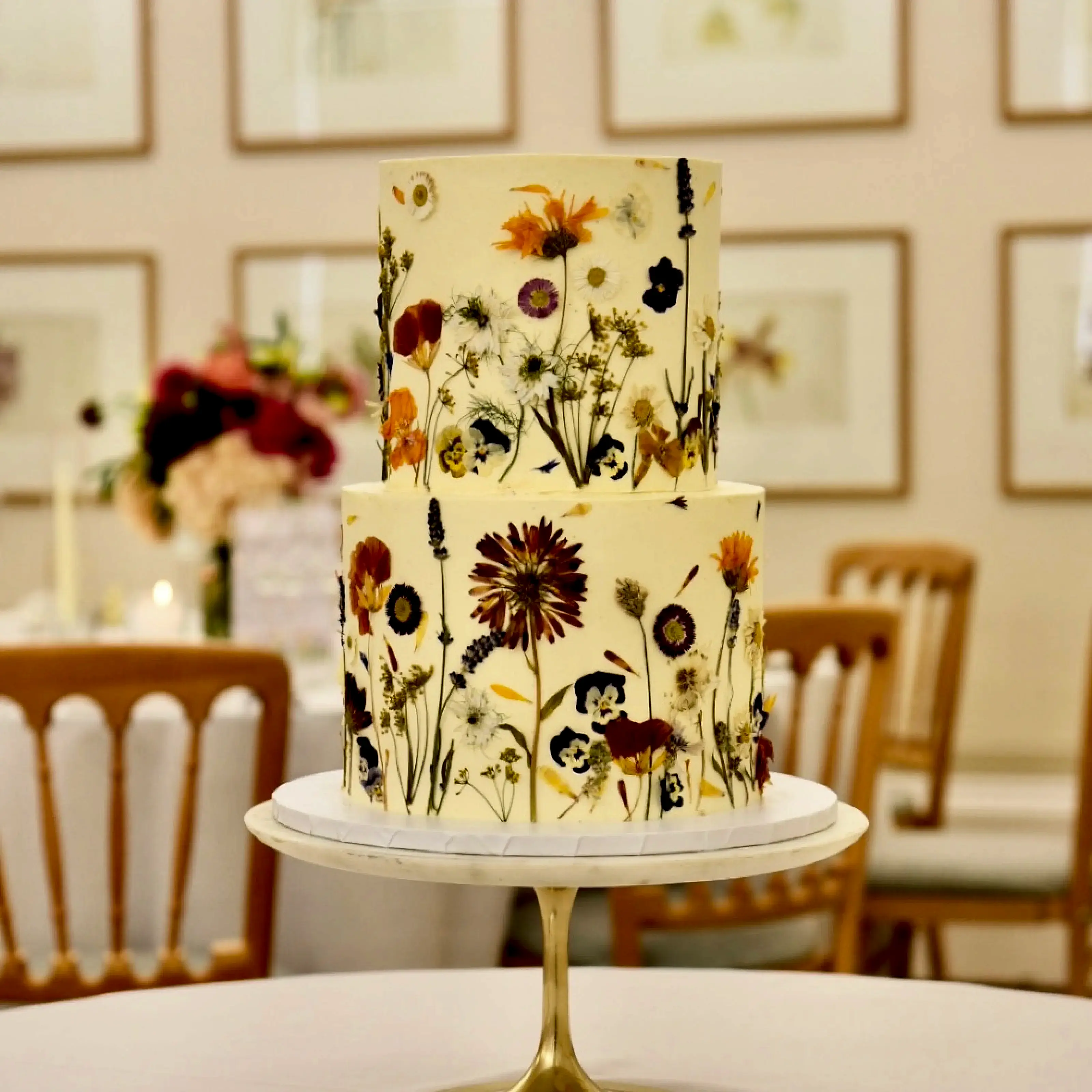A wedding cake decorated with edible flowers sits on a marble cake stand