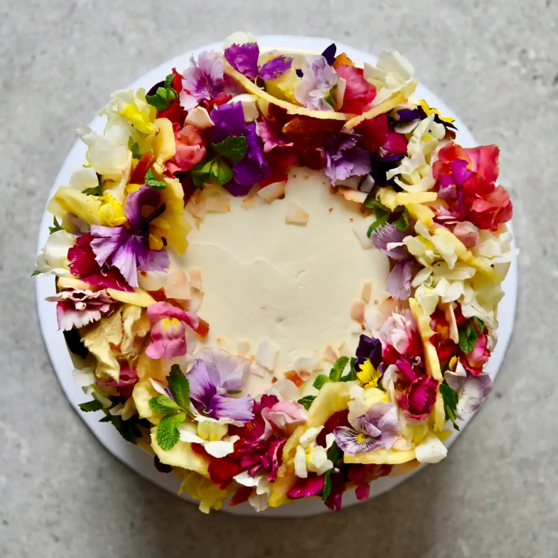 Pink, yellow and purple edible flowers on top of a wedding cake.