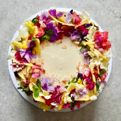 Pink, yellow and purple edible flowers on top of a wedding cake.