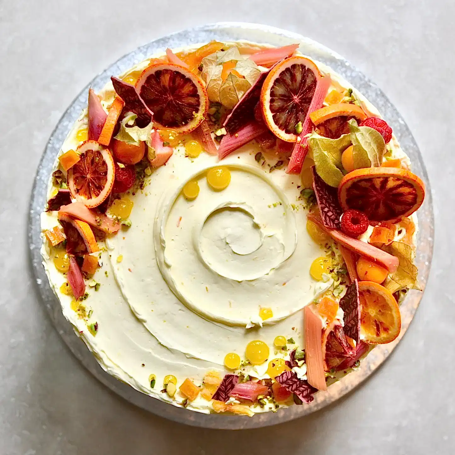 An overhead shot of a rhubarb flavoured cake decorated in vibrant reds and oranges natural flower and fruits.
